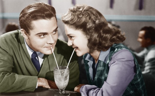 Couple in a restaurant looking at each other and sharing a milk shake with two straws