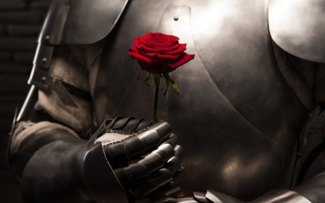 Closeup portrait of medieval knight in armor holding red rose on dark background, romance concept