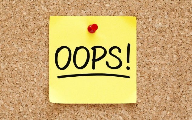 Oops! on yellow sticky note pinned with red push pin on cork board.