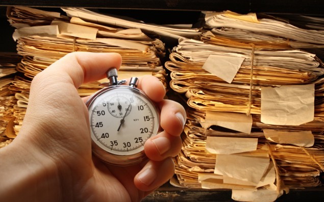 Hand with stopwatch, paper documents stacked in archive
