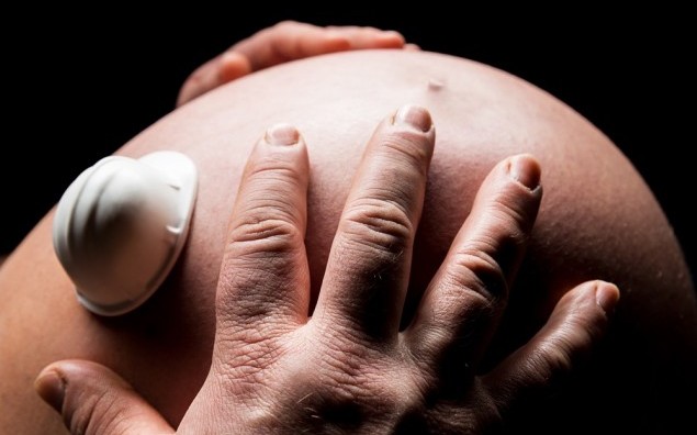 hands holding a belly of pregnant woman with worker helmet