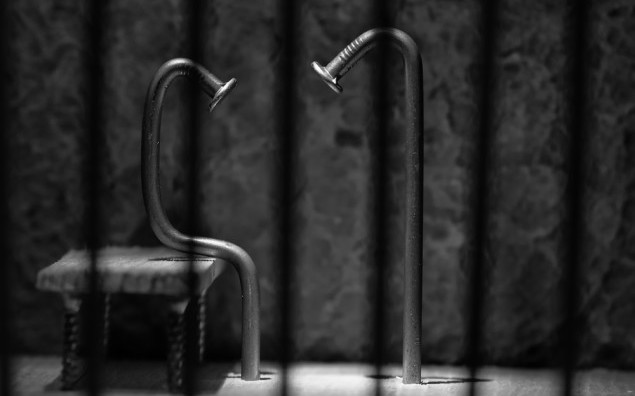 Conceptual jail photo with iron nail sitting behind bars artisti