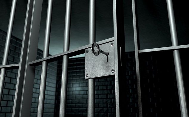 A closeup of the lock of a brick jail cell with iron bars and a key in the locking mechanism with the door open