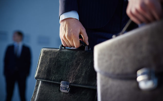 Cropped image of business partners carrying briefcases on the foreground while their colleague standing on the background
