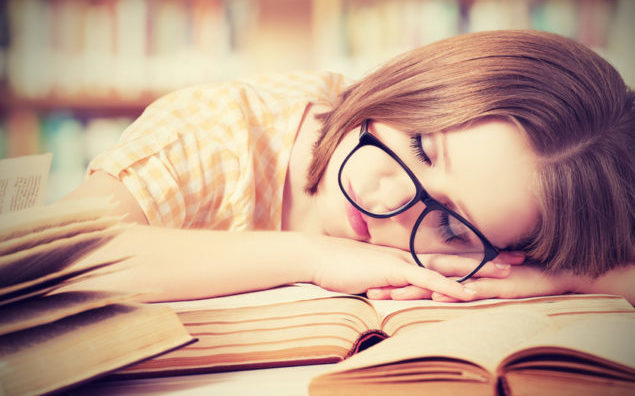tired student girl with glasses sleeping on books in library