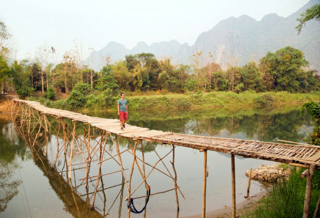 Cheerful Tourist crossing bamboo bridge, limestone view, laos